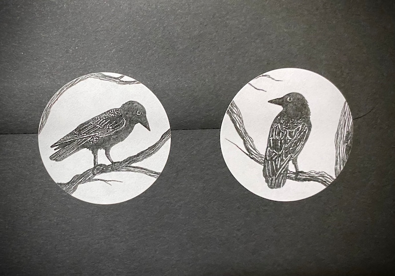 May include: Two black and white illustrations of crows perched on branches. The crows are drawn in a simple, stylized manner.