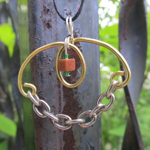 May include: A gold and silver necklace with a brown and green bead pendant. The pendant is suspended from a chain and has a geometric design.