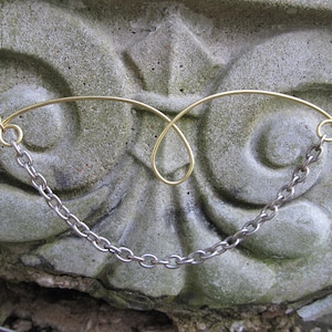 May include: A gold and silver chain necklace with a delicate gold wire design. The necklace is displayed on a textured stone surface.