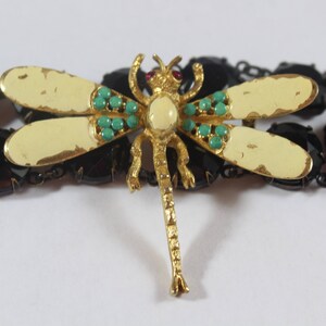May include: A gold dragonfly brooch with turquoise and red accents. The dragonfly is set against a background of black beads.