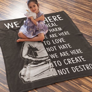 May include: A gray fleece blanket with the text "We are here to heal harm, we are here to love not hate, we are here to create not destroy".