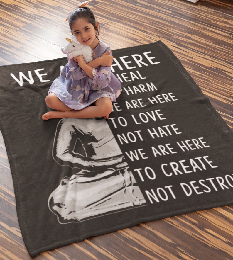 May include: A gray fleece blanket with the text "We are here to heal harm, we are here to love not hate, we are here to create not destroy".