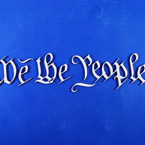 May include: White wooden letters spelling "We the People" on a blue background.
