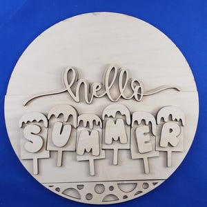K&ouml;nnte beinhalten: Runder Holzschild mit den ausgeschnittenen Worten "hello SUMMER". Das Wort "hello" ist kursiv geschrieben, und "SUMMER" ist in Blockbuchstaben gehalten, wobei jeder Buchstabe als Eis am Stiel gestaltet ist. Das Schild ist aus unbehandeltem Holz.