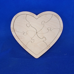 May include: A wooden heart-shaped puzzle with a simple design. The puzzle is made of five pieces and has a decorative border of leaves.