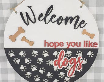 May include: Round wooden sign with the word "Welcome" in black script. The sign has a white top half and a black bottom half with paw prints. The words "hope you like dogs" are in red and white. Includes three bone accents.