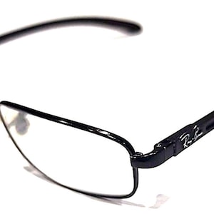 May include: Black rectangular eyeglasses with clear lenses. The frames are a glossy black, with the Ray-Ban logo on the temples. The glasses have a modern, minimalist design, suitable for everyday use.
