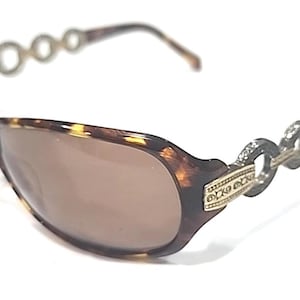 Puede incluir: Gafas de sol con estampado de carey y lentes marrones. Las patillas presentan un diseño de cadena plateada decorativa. Las monturas también tienen un acento dorado con un patrón grabado. Un accesorio de moda para la protección ocular.