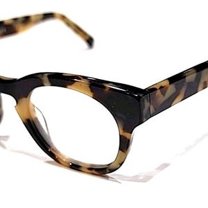 May include: A pair of eyeglasses with a tortoiseshell pattern. The frames are a mix of brown, tan, and black, with a rounded shape and clear lenses. The temples are also tortoiseshell, and the glasses are set against a white background.