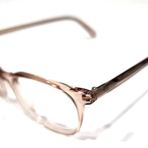 May include: A pair of eyeglasses with a light brown frame and temples. The lenses are clear, and the frame has a subtle, translucent quality. The glasses are set against a white background.