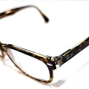 May include: A pair of Ray-Ban eyeglasses with a tortoiseshell pattern on the frames. The glasses have a classic rectangular shape and clear lenses. The Ray-Ban logo is visible on the temple. The glasses are set against a white background.