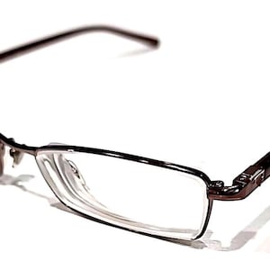 May include: Rectangular eyeglasses with a dark brown frame and clear lenses. The glasses have a classic design with a thin frame and temples. The lenses are rectangular, and the overall style is modern and understated.