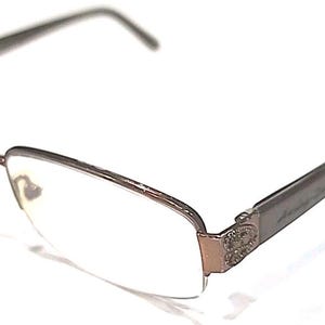 May include: A pair of eyeglasses with a brown metal frame and clear lenses. The rectangular lenses are set in a thin frame with a decorative element at the temple. The arms are a darker brown colour.