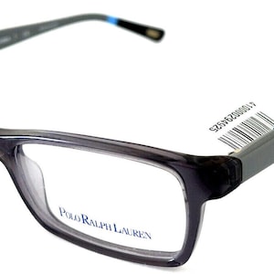 May include: Gray rectangular Polo Ralph Lauren eyeglasses. The frames are a dark gray with a subtle gradient. The temples are a darker gray with a blue logo. The lenses are clear. A white tag with a barcode is attached to the left temple.