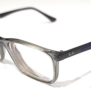 May include: Ray-Ban spectacles with a grey gradient frame and black arms. The Ray-Ban logo is visible on the arm. The glasses have a rectangular shape and clear lenses.