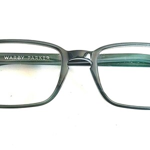 May include: Black rectangular eyeglasses with green lenses and the text "Warby Parker" on the frame.