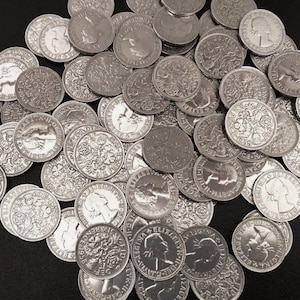 Könnte beinhalten: Eine Ansammlung silberner Münzen, jede mit einem Profil und floralen Mustern. Die Münzen sind verstreut und zeigen ihre detaillierten Designs und ihren metallischen Glanz. Die Münzen scheinen alt zu sein, mit sichtbaren Inschriften.