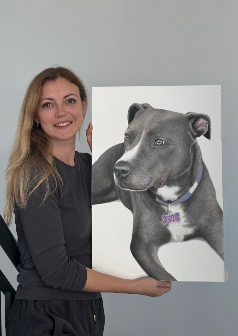 May include: A portrait of a gray dog with a white patch on its face, wearing a purple collar and a tag that says "Eve". The artwork is held by a person with long blonde hair.
