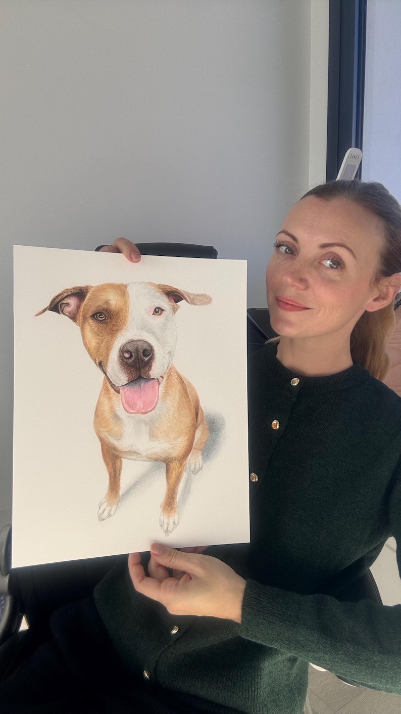May include: A detailed color pencil drawing of a brown and white dog with a pink tongue. The dog is sitting and looking directly at the viewer. The artwork is on white paper.