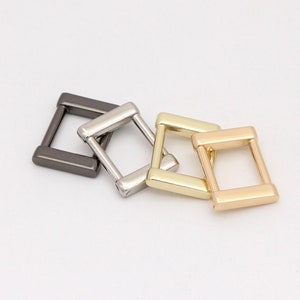 May include: Four metal square buckles in varying metallic finishes: dark gray, silver, gold, and light gold. The buckles are arranged diagonally, showcasing their geometric design and smooth, polished surfaces. Ideal for crafting and accessories.