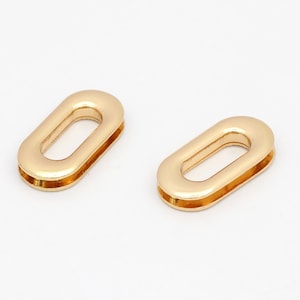 Puede incluir: Dos anillos ovalados de metal de color dorado con un agujero en el centro. Los anillos son lisos y brillantes.