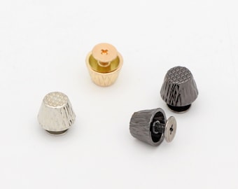 Könnte beinhalten: Drei metallene Schraubkappen in Gold, Silber und Schwarz. Die Kappen haben ein strukturiertes, geriffeltes Design.