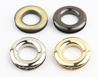 May include: Four metal eyelets in antique brass, gunmetal, silver, and gold finishes. The eyelets are 18mm in diameter and have a rounded shape. They are arranged in a square formation against a white background.