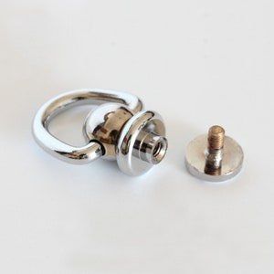 May include: A silver swivel snap hook with a round base and a screw-on attachment. The hook is designed for attaching to a strap or other item.