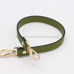 May include: A green leather strap with gold hardware and two swivel hooks. The strap is approximately 1 inch wide.