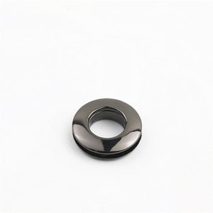 May include: A black metal grommet with a smooth, shiny finish. The grommet has a round shape with a hole in the center.