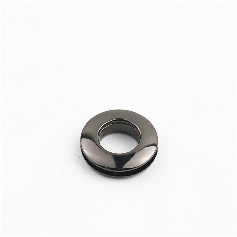 May include: A black metal grommet with a smooth, shiny finish. The grommet has a round shape with a hole in the center.
