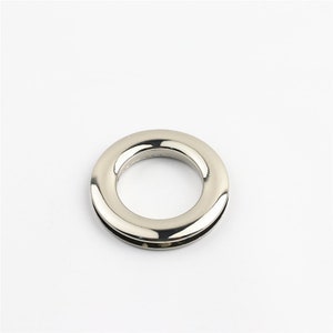 May include: A silver metal ring with a smooth, polished finish. The ring has a large inner diameter and a smaller outer diameter, creating a raised edge.