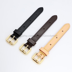 May include: Three leather straps in black, brown, and tan, each with a gold-coloured buckle. The straps are of varying shades, with the black being the darkest and the tan the lightest. The buckles are rectangular with a rounded edge.