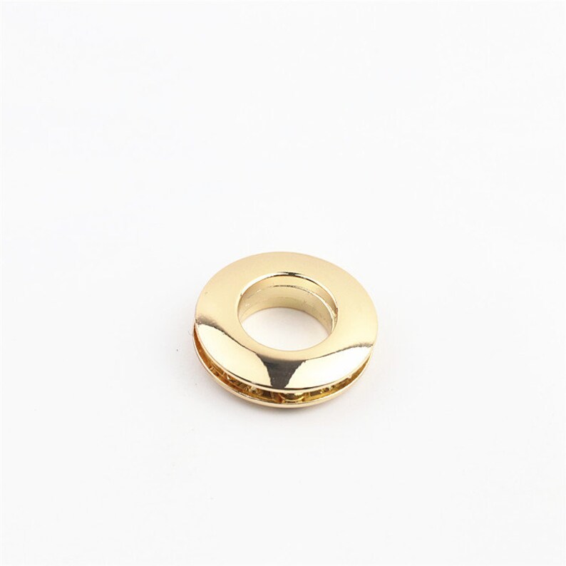 May include: A gold-colored metal grommet with a smooth, shiny finish. The grommet has a circular shape with a hole in the center.