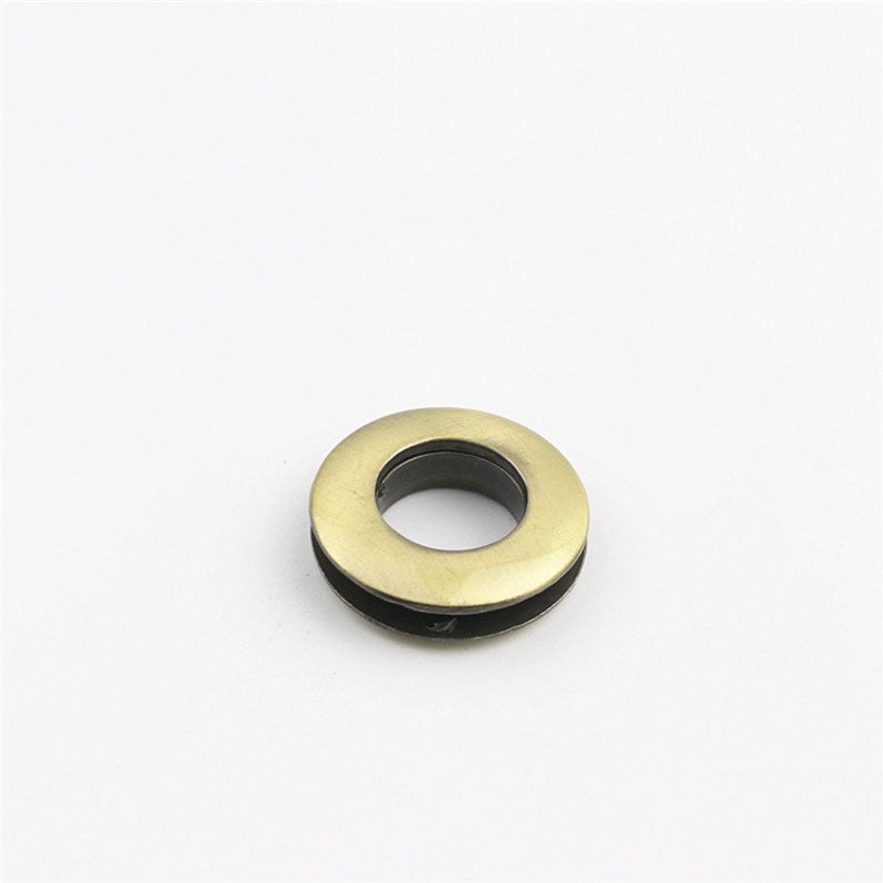 May include: A gold metal grommet with a black inner ring. The grommet is a circular shape with a hole in the center.