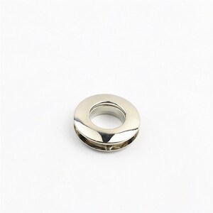 May include: Silver metal grommet with a smooth, shiny finish. The grommet has a round shape with a hole in the center.