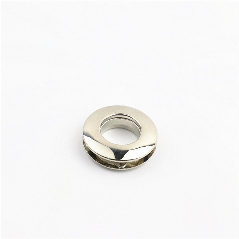 May include: Silver metal grommet with a smooth, shiny finish. The grommet has a round shape with a hole in the center.