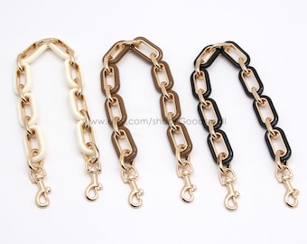 May include: Three handbag chain straps in ivory, brown, and black, each with gold-tone metal links and lobster claw clasps. The chains are displayed against a white background, showcasing their color variations.