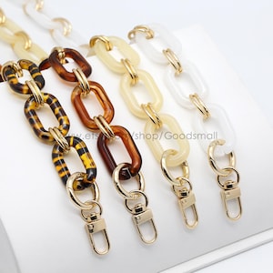 May include: Three different styles of chain bag straps. The first strap is brown and black with a leopard print pattern. The second strap is a pale yellow colour. The third strap is white. All three straps have gold metal clasps.