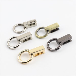 Könnte beinhalten: Fünf Metall-Schwenkverschlüsse mit einem Ring und einer rechteckigen Stange. Die Verschlüsse sind in verschiedenen Ausführungen: Silber, Gold, Antikmessing und Schwarz.