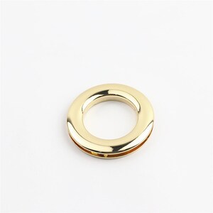 May include: A gold-colored metal ring with a smooth, polished finish. The ring is designed for attaching to fabric or leather.