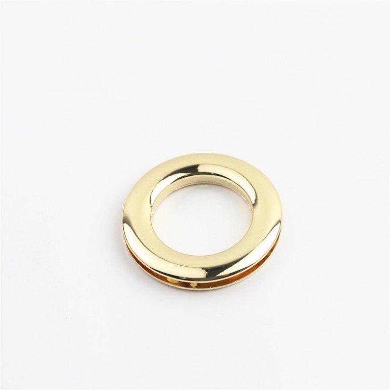 May include: A gold-colored metal ring with a smooth, polished finish. The ring is designed for attaching to fabric or leather.