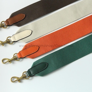 May include: Four colorful bag straps in brown, off-white, orange, and green. Each strap has a leather end piece and a gold-colored metal clasp. The straps are angled diagonally across a white background.