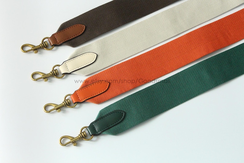 May include: Four colorful bag straps in brown, off-white, orange, and green. Each strap has a leather end piece and a gold-colored metal clasp. The straps are angled diagonally across a white background.