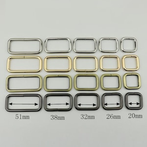 May include: Five rows of rectangular metal rings in silver, gold, bronze, and black. The rings are arranged in decreasing size from left to right. The rings are 51mm, 38mm, 32mm, 26mm, and 20mm in size.