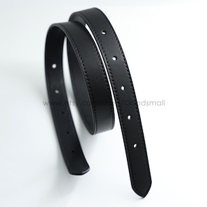 May include: A slim black leather belt coiled in a circular shape. The belt features a smooth matte finish with visible tonal stitching along both edges and a series of evenly spaced circular adjustment holes running along the length of the strap.