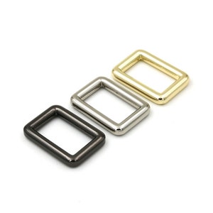 May include: Three metal D-rings in different finishes: black, silver, and gold. The rings are rectangular in shape and have a smooth, polished finish.