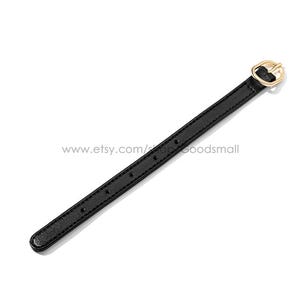 May include: Black leather strap with a gold-colored buckle. The strap has several holes for adjustment and a rounded end. The buckle is a simple, elegant design. The strap is set against a white background.