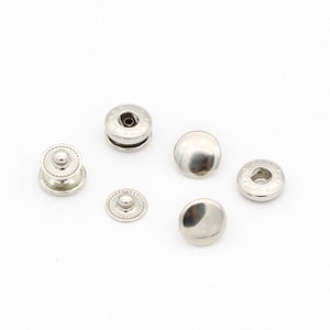 May include: A set of six silver-toned snap fasteners. The fasteners are round and have a smooth, shiny finish. They are designed for use in clothing and other fabric projects.