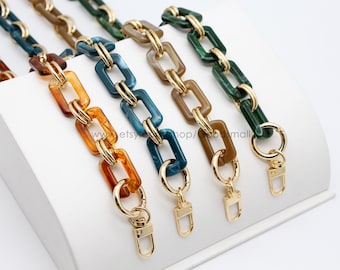 May include: Four different colored plastic chain bag straps with gold metal clasps. The chains are made of square links with a marbled effect. The colors are teal, brown, green, and orange.